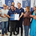 Homens e mulheres em pé sorriem para a câmera enquanto dois deles seguram um documento