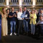 Homens e mulheres estão em pé, lado a lado, sorrindo e aplaudindo