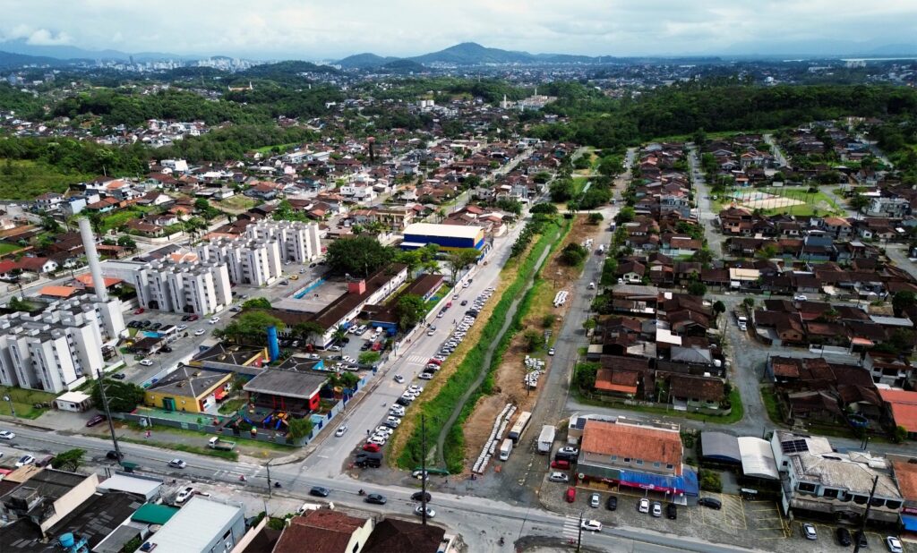 Imagem aérea mostra rio, ruas, imóveis e vegetação na área em que será construído o Passeio Público do Parque Guarani