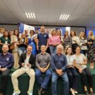 Homens e mulheres sentados e em pé em palco seguram troféus e sorriem