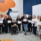 Homens e mulheres em pé, além de um homem em cadeira de rodas, posam para foto segurando papel branco