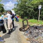 Pessoas com luvas manipulam resíduos descartados incorretamente em área às margens de rio