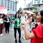 Mulher com fone de ouvido e microfone fala para plateia em pé em praça