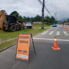 Imagem mostra uma rua asfaltada parcialmente interditada com cones que impedem a passagem de veículos. Há uma placa indicando que há obras e máquinas estacionadas no terreno ao lado