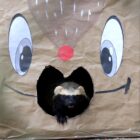 Um furão de cores preta e marrom está dentro de uma caixa de papelão decorada remetendo a uma rena