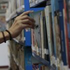 Mão de pessoa pega um livro em prateleira de livros em biblioteca