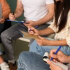 Três pessoas não identificadas sentadas com caneta e papel nas mãos