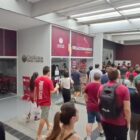 Várias pessoas estão caminhando em uma mesma direção dentro de um prédio em cores branco e vermelho