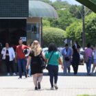 Dezenas de pessoas estão em movimento na entrada de uma universidade, algumas em direção à saída e outras à entrada