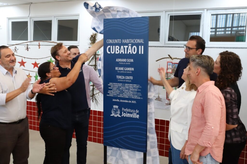 Homens e mulheres estão ao redor de placa com o termo Conjunto Habitacional Cubatão II e sorreim