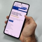 Mão masculina segura celular com tela do site da prefeitura de Joinville em página intitulada Consulta Pública para Inovação Aberta