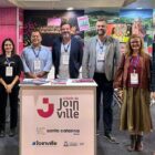 Duas mulheres e cinco homens posam para foto e sorriem em stand de Joinville em feira de negócios