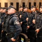 Homens uniformizados e portado armas longas estão enfileirados em duas filas, sérios e com olhar à frente