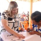 Mulher idosa assina documento em uma mesa enquanto mulher a orienta ao lado