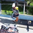 Homem, com equipamentos de segurança, trabalha em equipamento suspenso em manutenção de poste de iluminação pública