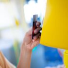 Imagem mostra uma mão segurando um cartão e passando pelo dispositivo de leitura de um ônibus