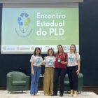 Mulher recebe prêmio e sorri para foto em palco, ao lado de outras três mulheres