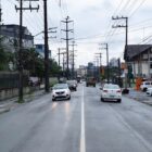Rua asfaltada com faixa branca no centro e um carro seguindo em cada direção
