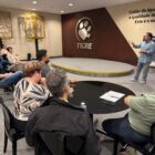 Homem em pé fala para plateia sentada