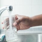 Mão segura copo de vidro abaixo de torneira aberta com água