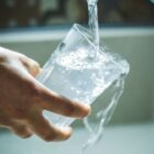 Mão segura copo de vidro abaixo de torneira aberta com água