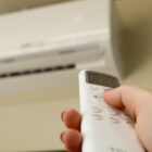 Mão com controle remoto aponta para aparelho de ar-condicionado instalado na parede