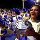Foliões, crianças e adultos, com fantasias em desfile de Carnaval tocam instrumentos musicais