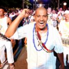 Foliões vestidos de branco sorriem enquanto desfilam na avenida