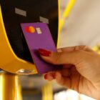 Mão de mulher com unhas vermelhas aproxima cartão de crédito do dispositivo de leitura dentro de um ônibus