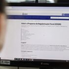 Mulher olha para tela de computador com informações sobre programa de regularização fiscal