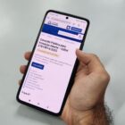 Mão de homem segura celular e na tela há informações sobre consulta pública