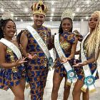 Três mulheres e um homem com faixas de rei, rainha e princesas do Carnaval, coroas e figurino, posam para foto