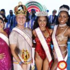 Imagem mostra um homem e três mulheres em pé, com figurino carnavalesco, faixas e coroas, sorrindo para a câmera