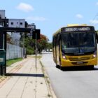 ônibus amarelo trafega em rua perto de ponto de parada de transporte coletivo