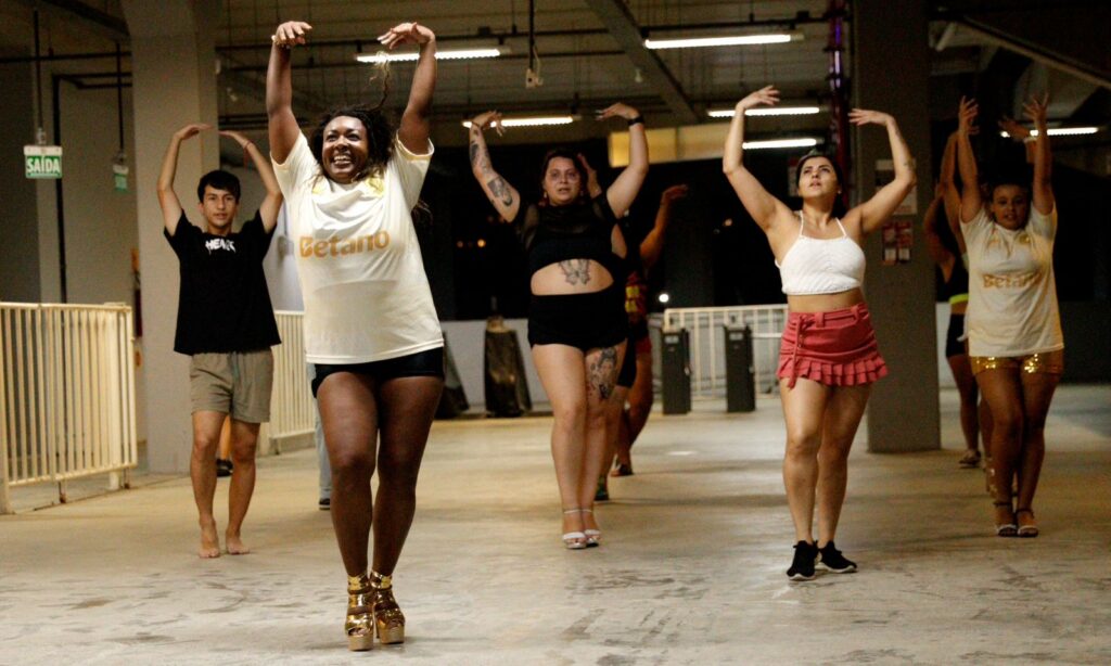 Quatro mulheres e um homem dançam com os braços para cima