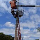 Homem uniformizado e com equipamentos de proteção trabalha em escada para acessar um poste