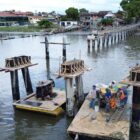 Homens com equipamentos de segurança, trabalham em plataforma em lagoa