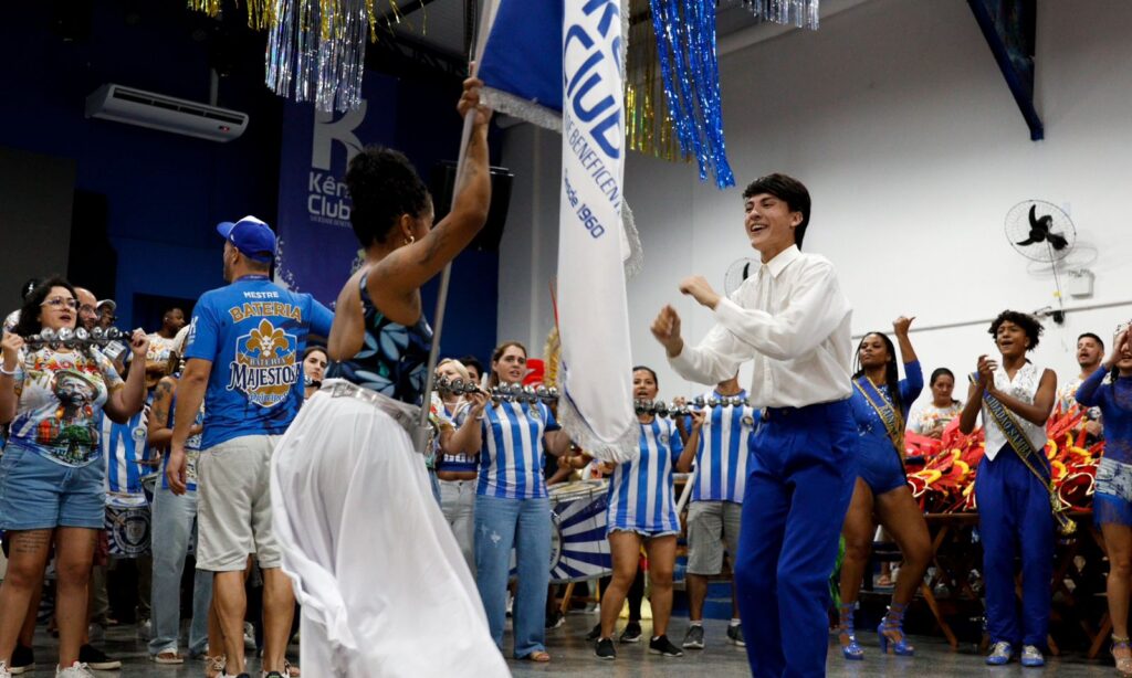 Homem branco e mulher negra jovens dançam enquanto ela segura uma bandeira