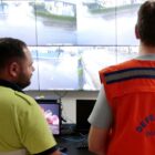 Dois homens de costas olham para telas com imagens em tempo real