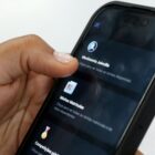 Mão negra segura celular com tela aberta no aplicativo Joinville Fácil