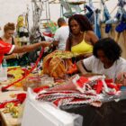 Mulheres estão ao redor de uma mesa onde confeccionam fantasias