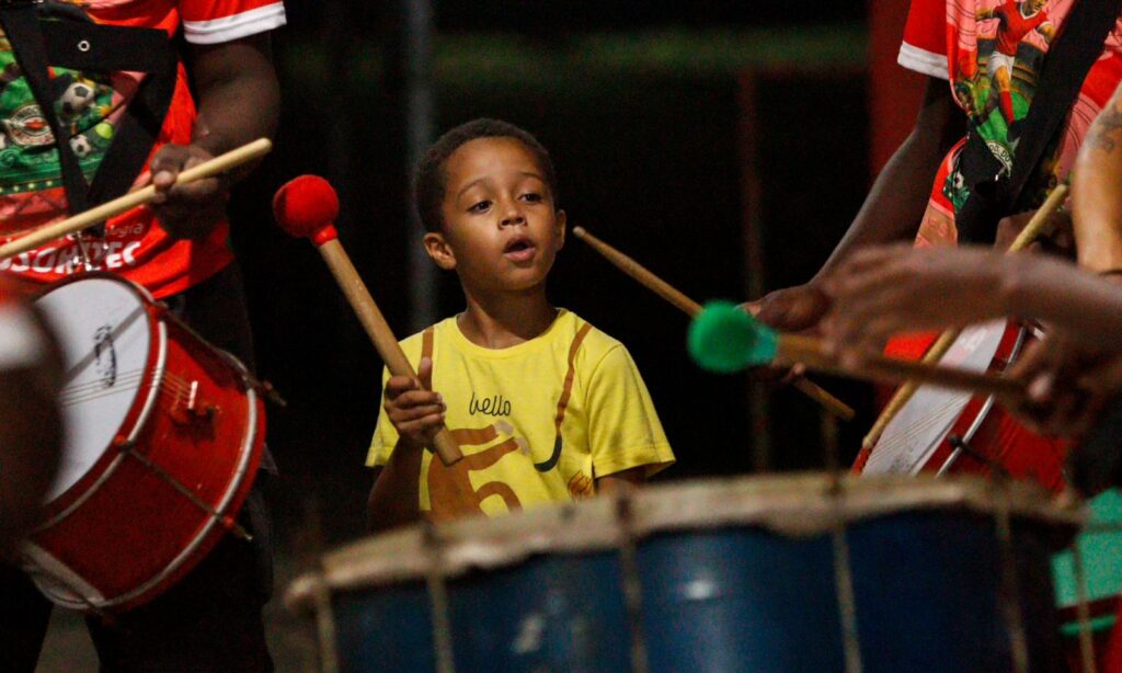 Menino de camisa amarela toca instrumento de percussão