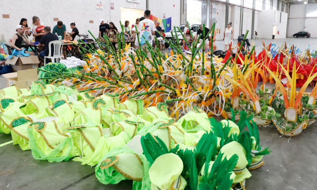 Fantasias verdes, amarelas e coloridas estão posicionadas no chão de um amplo galpão