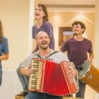 Cinco pessoas com sanfona e instrumentos de percussão se apresentam