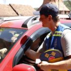 Homem com boné e colete entrega folder para motorista dentro de carro