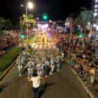Desfile de Carnaval com passistas e carros e público assistindo