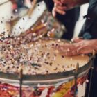 Imagem mostra duas mãos tocando instrumento de percussão com confetes de Carnaval