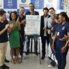 Pessoas batem palma ao redor de uma placa de inauguração