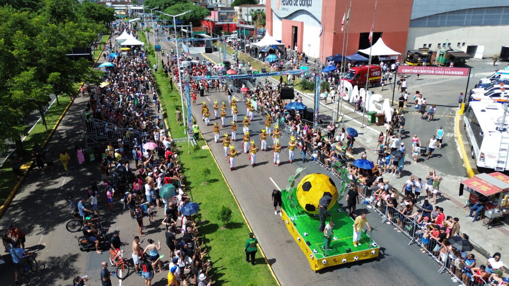 Visão aérea de desfile mostra carro alegórico com grande bola amarela