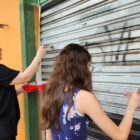 Duas mulheres pintam a porta de um comércio
